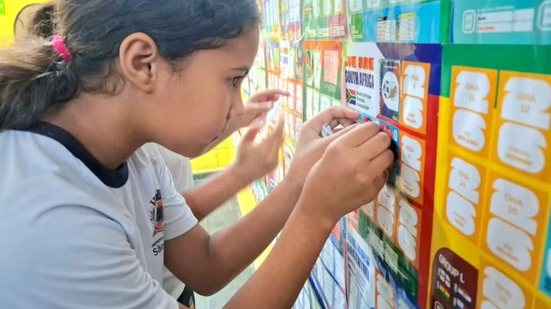 Alunos do Amei Maria de Lourdes Batista, em São Vicente, participam de projeto coletivo com álbum da Copa do Mundo fixado na parede do pátio da escola - Imagem: Prefeitura de São Vicente/Divulgação