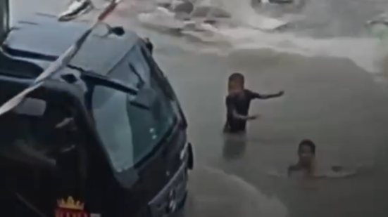 Crianças brincando em água suja enfrentam risco de atropelamento por caminhão em Guarujá durante chuvas intensas - Imagem: Reprodução/ Guarujá Mil Grau